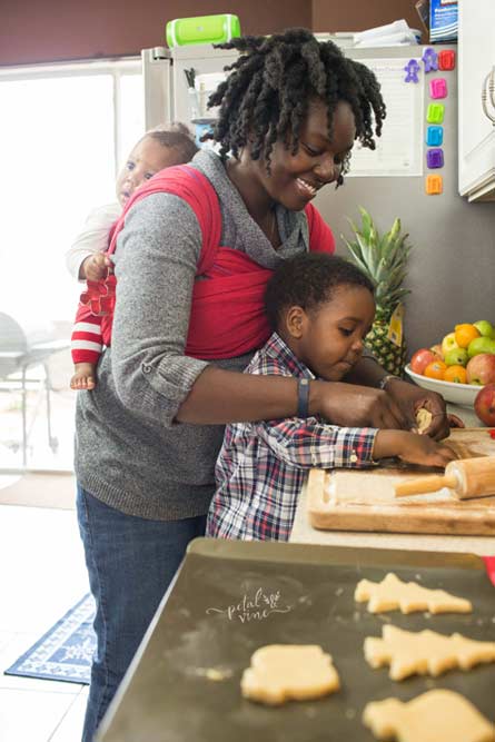 Baby wrapped on back while mom bakes with big brother