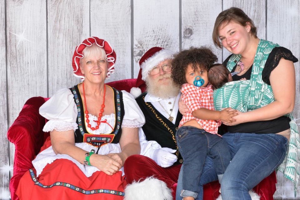 Newborn in baby wrap while mom holds toddler on Santa's lap